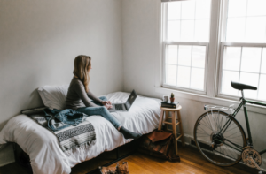 young woman sitting on bed working from home on laptop