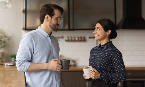 Colleagues in workplace kitchen standing with a cup of coffee