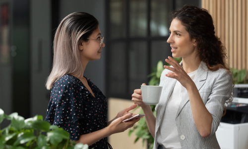 2 women standing in office kitchen with coffee cups